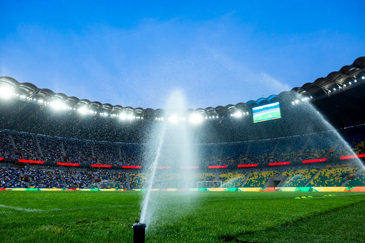 our-services-1 Nighttime view of a soccer stadium with sprinklers watering the field, enhancing the vibrant atmosphere.